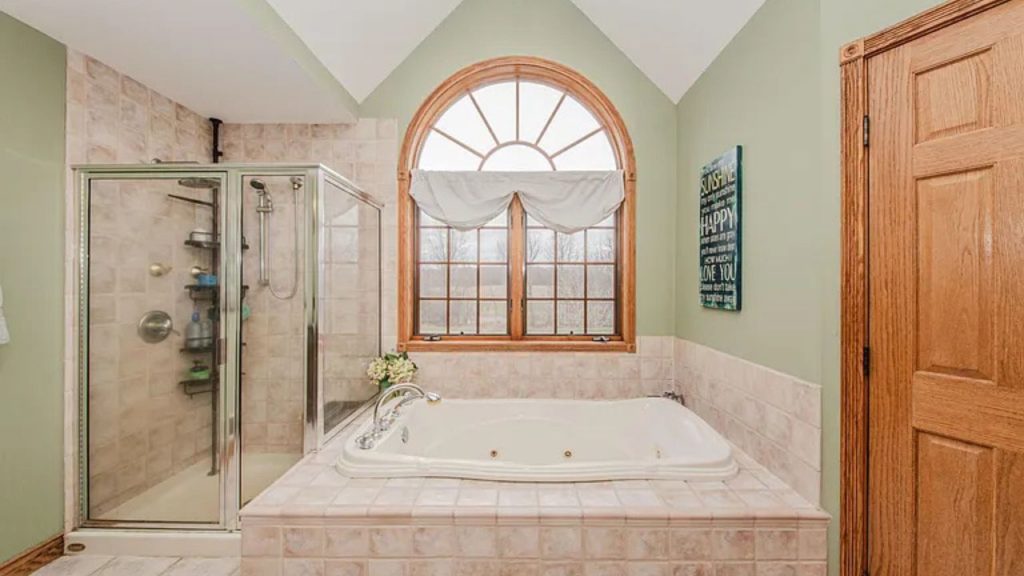 A peaceful bathroom with a jetted tub, glass shower, and large arched window.