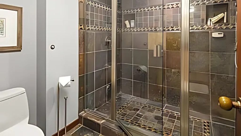 Slate-tiled walk-in shower with glass doors and mosaic accents.