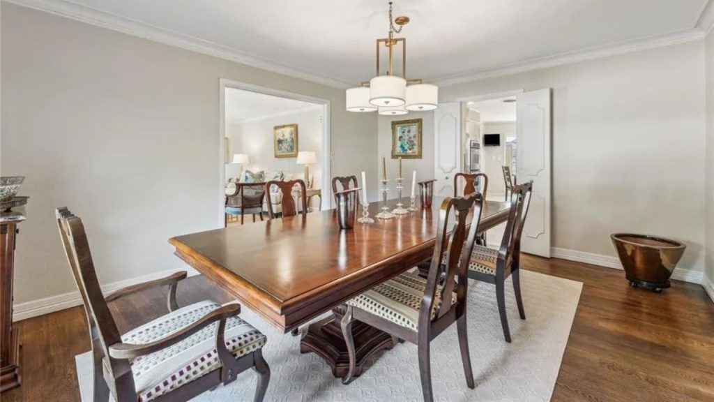 A warm dining room with a wooden table, elegant chairs, a chandelier, and artwork, opening to a living area.