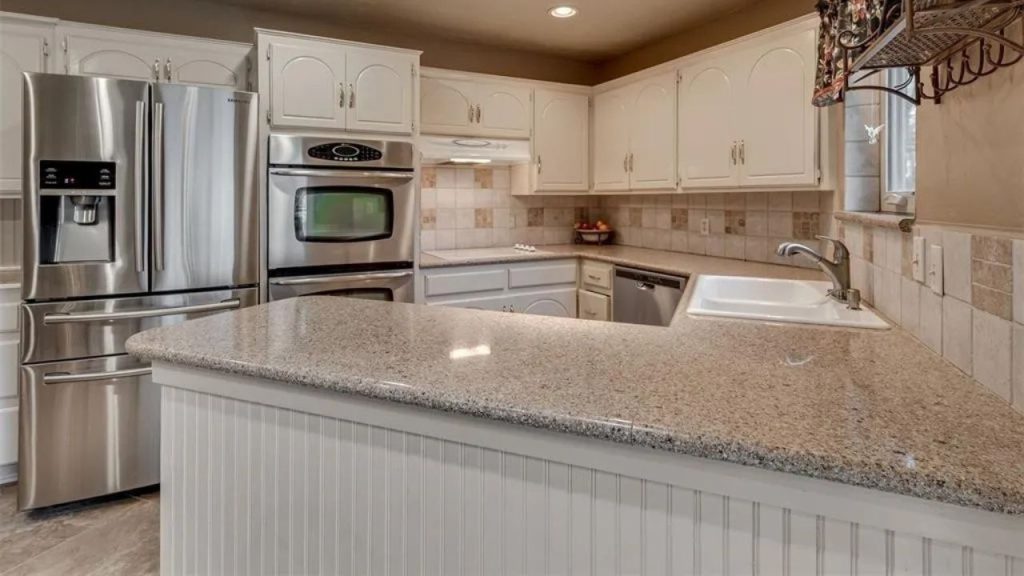 Bright kitchen with granite countertops, stainless steel appliances, white cabinets, and a cozy island, lit by natural light.