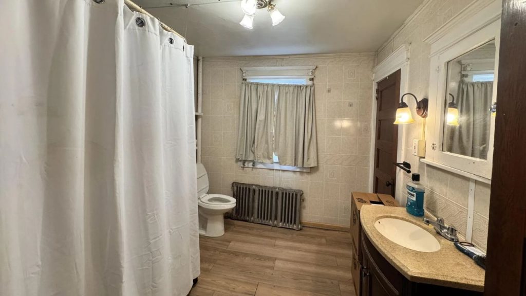 A cozy bathroom with wooden floors, a shower curtain, small window, and granite vanity.