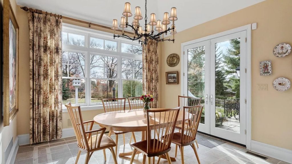A sunny breakfast nook with a wooden table, chandelier, and large windows.