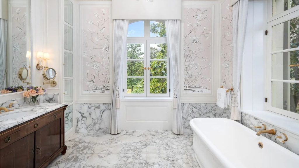 A serene bathroom with a marble tub, floral wallpaper, and large windows.