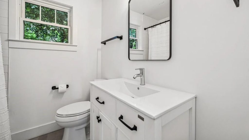 A bright bathroom with a white vanity, single sink, and window overlooking greenery.
