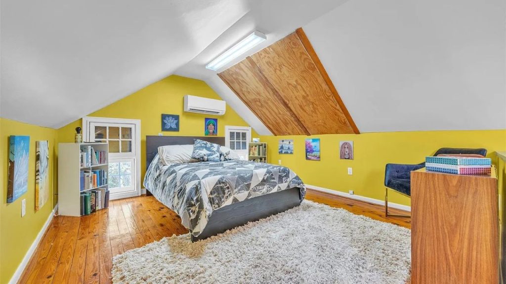 An inviting attic bedroom with yellow walls, a gray bed, white rug, and slanted wooden ceiling.