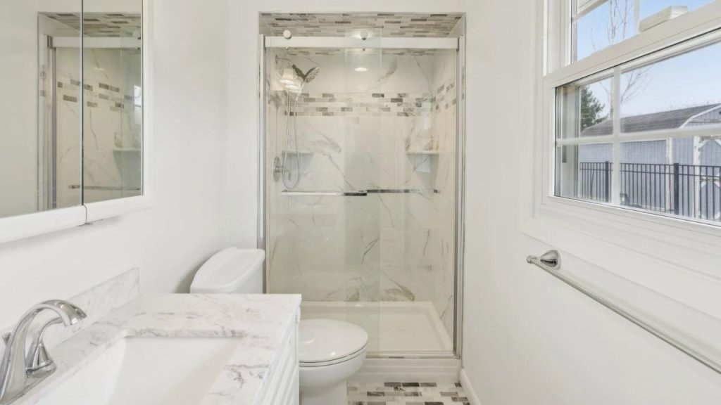 A serene bathroom with a glass shower, marble vanity, and large window, featuring modern tiles and fixtures.