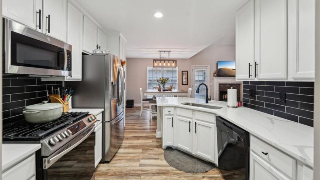 A bright kitchen with white cabinets, black tile backsplash, stainless steel appliances, and a dining area.