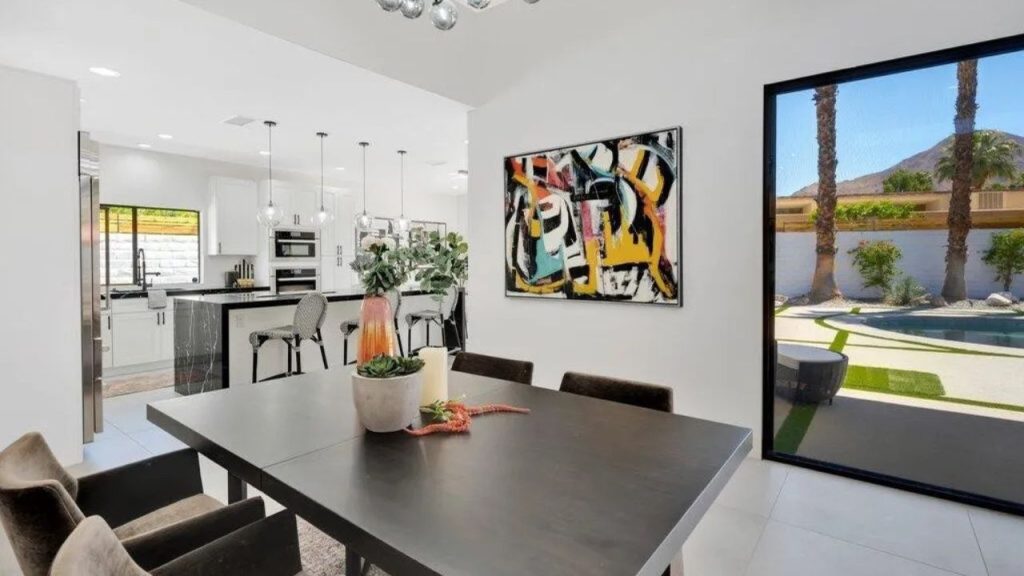 A chic dining area with a dark wood table, abstract art, and views of a pool and palm trees.