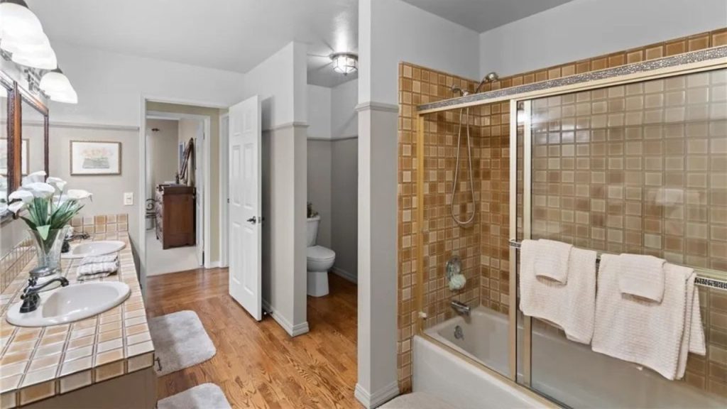 A peaceful master bathroom with dual vanity, beige tiled shower, bathtub, and hardwood floors.