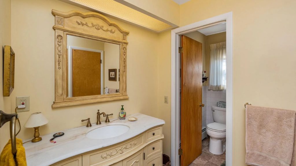 Vintage-style bathroom with ornate mirror, brass fixtures, and soft yellow walls.
