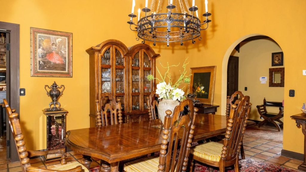 Traditional dining room with carved wooden furniture, a wrought-iron chandelier, and warm golden walls.
