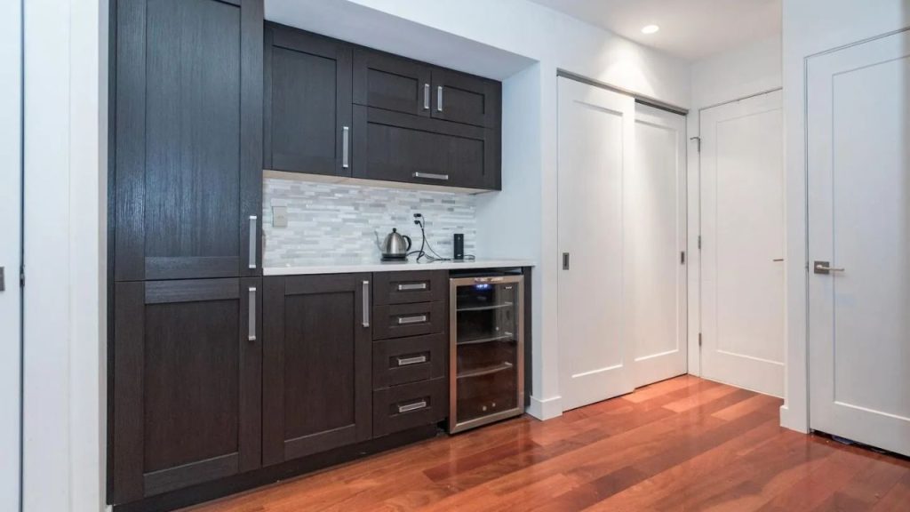 Small dark-wood kitchenette with a beverage fridge and white tile backsplash.