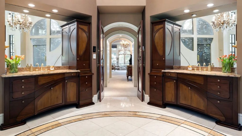 Elegant dual vanity with rich wood cabinetry, chandeliers, and arched doorways.