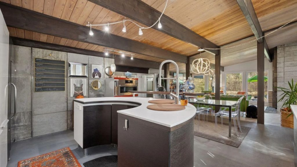 Open kitchen with wood ceiling, curved island, and glass dining table.