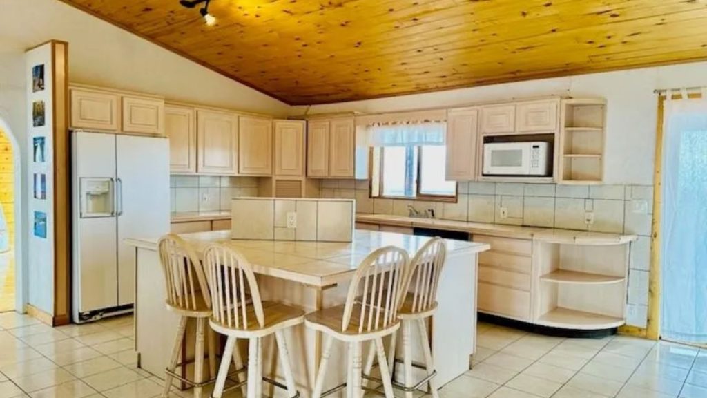 Bright kitchen with tiled island, light wood cabinets, and vaulted pine ceiling.