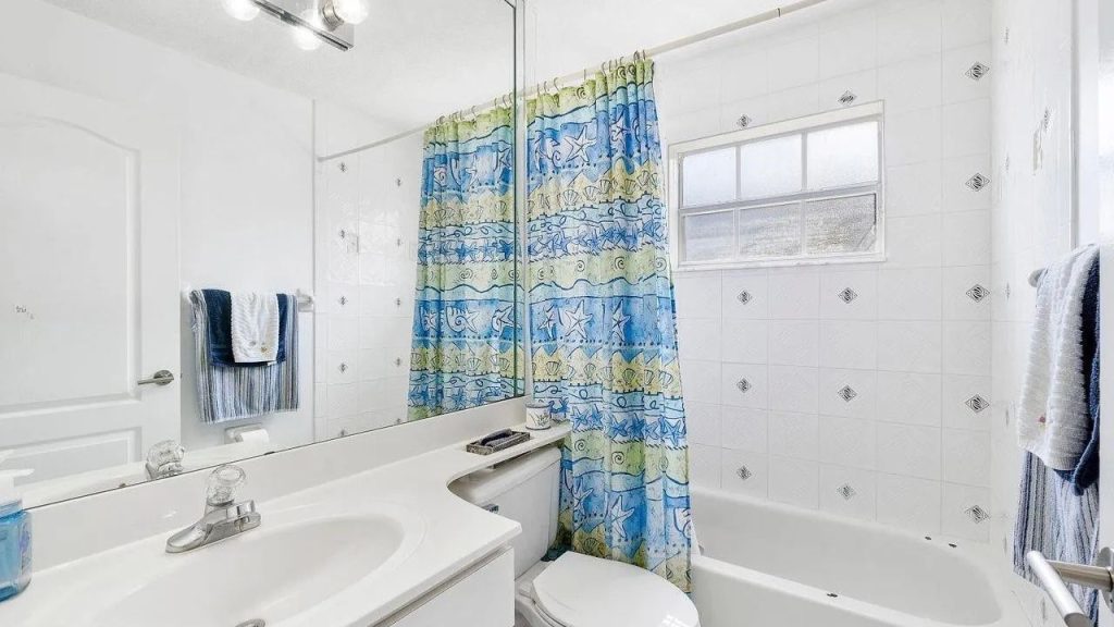 A bright bathroom with white tiles, a colorful shower curtain, and a large mirror.