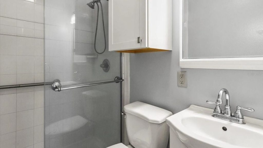 A minimalist bathroom with gray walls, white subway tiles, a glass shower, a white cabinet, and a large sink with chrome fixtures.