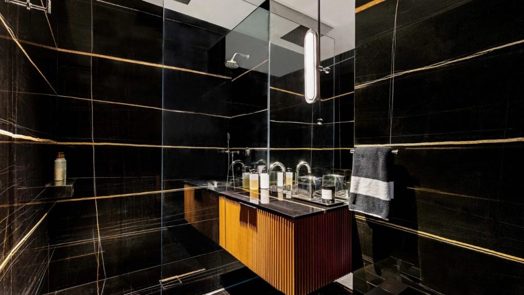 Sleek black bathroom with gold-veined tiles and wood-accented vanity.