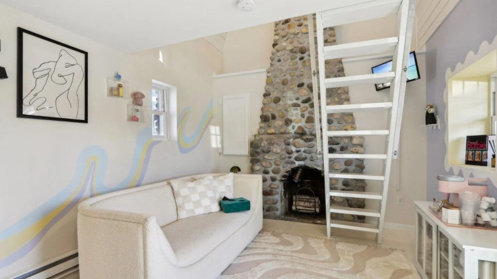 Cozy living nook with stone fireplace, loft ladder, and artistic pastel wall design.