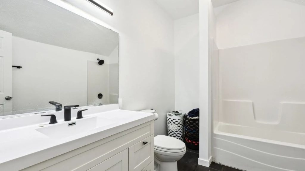 Bright bathroom with black fixtures, white vanity, and built-in tub.