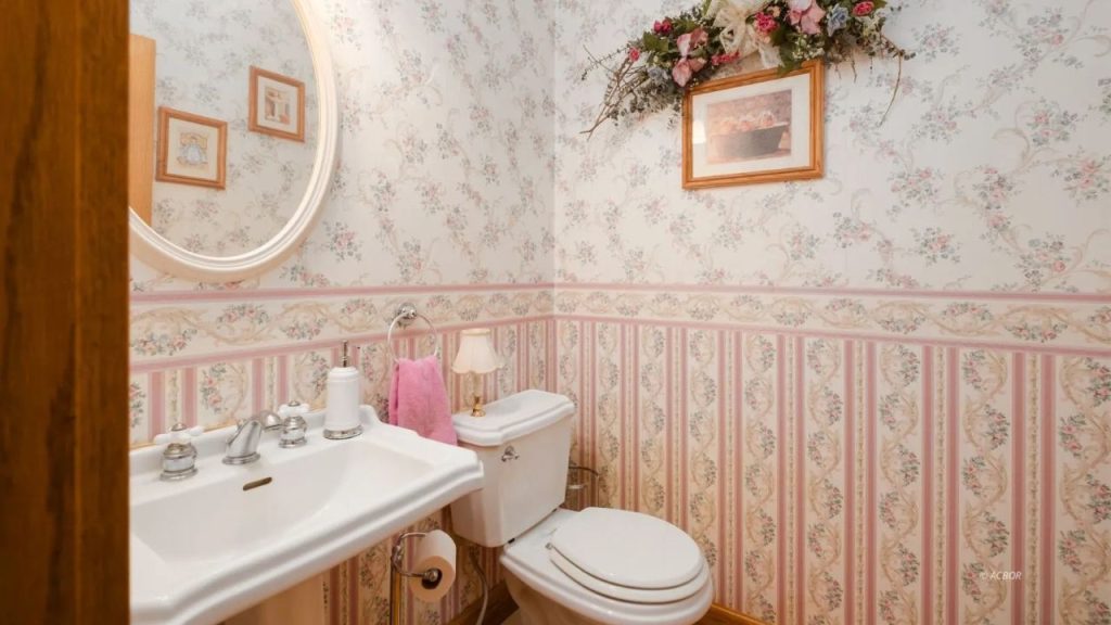 Vintage-style powder room with floral wallpaper, a pedestal sink, and soft pink accents.
