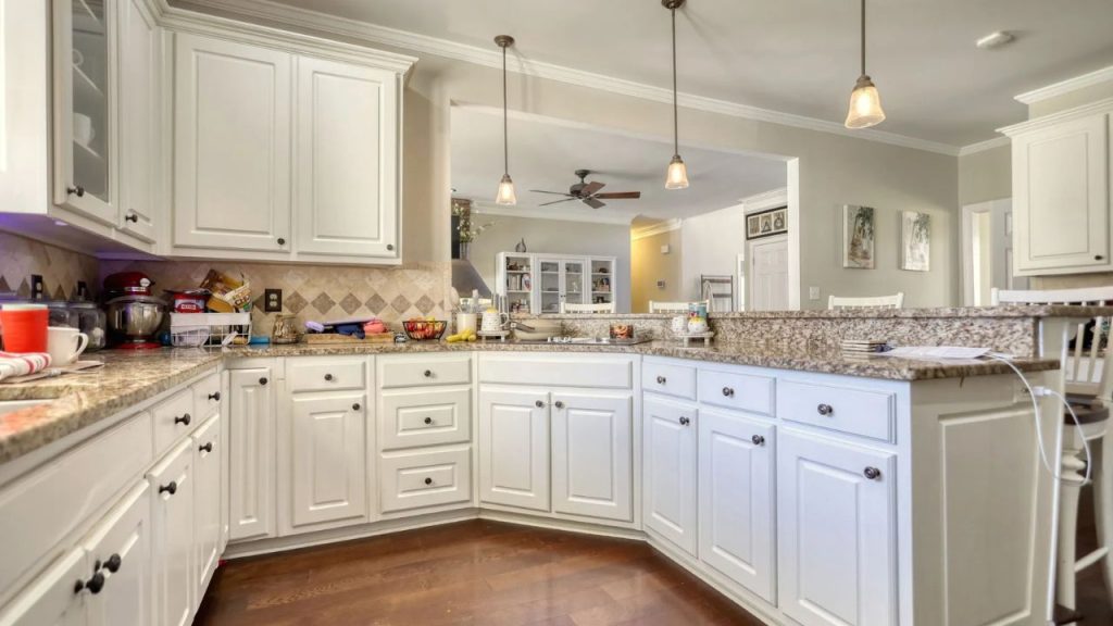 U-shaped kitchen with white cabinets, granite counters, and open view to living area.