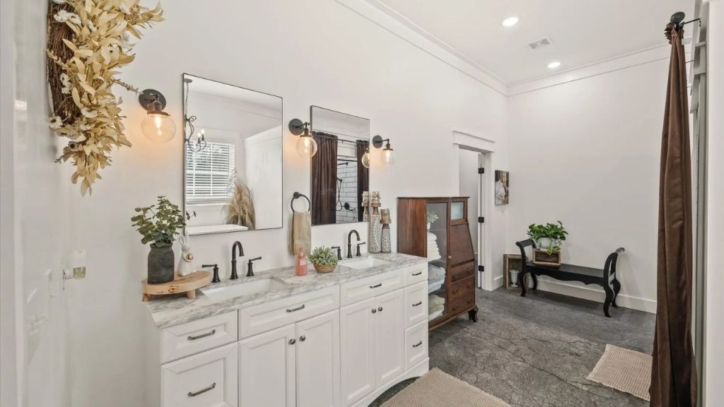 Bright farmhouse-style bathroom with a double vanity, black fixtures, and vintage storage cabinet.