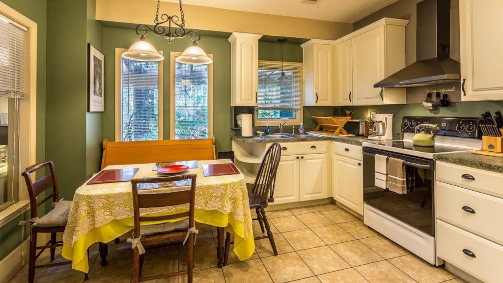 Warm kitchen with green walls, white cabinets, and a cozy window-side breakfast nook.