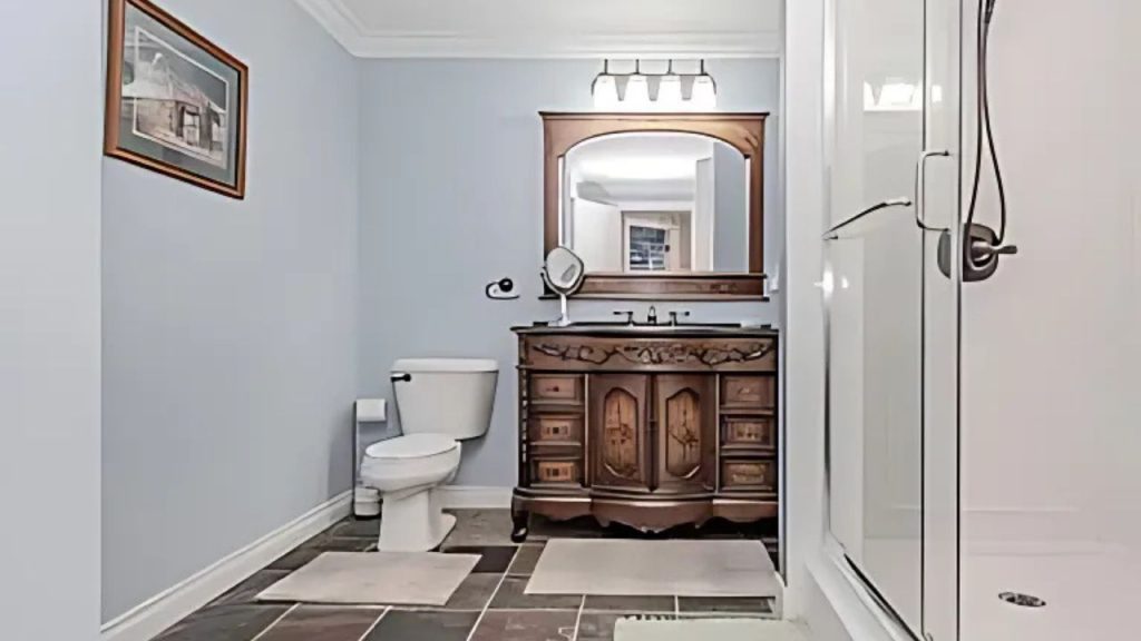 A classic bathroom with a wooden vanity, glass shower, and slate tiles.