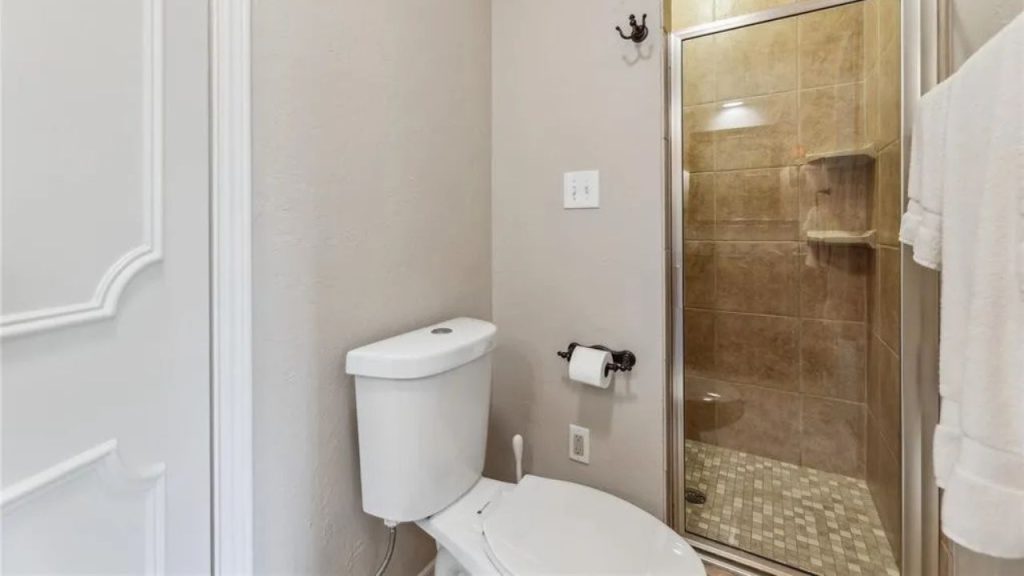 A small bathroom with a glass shower, white toilet, beige walls, and tan tiles, featuring a cozy design.