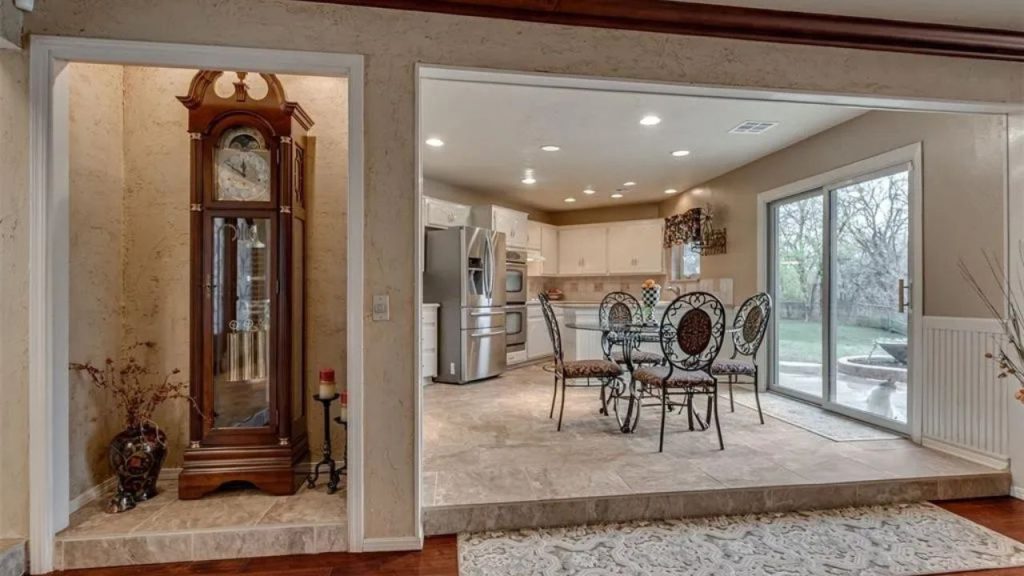 Cozy kitchen nook with a grandfather clock, dining table, and sliding doors to a backyard, featuring tiled floors and white cabinets.