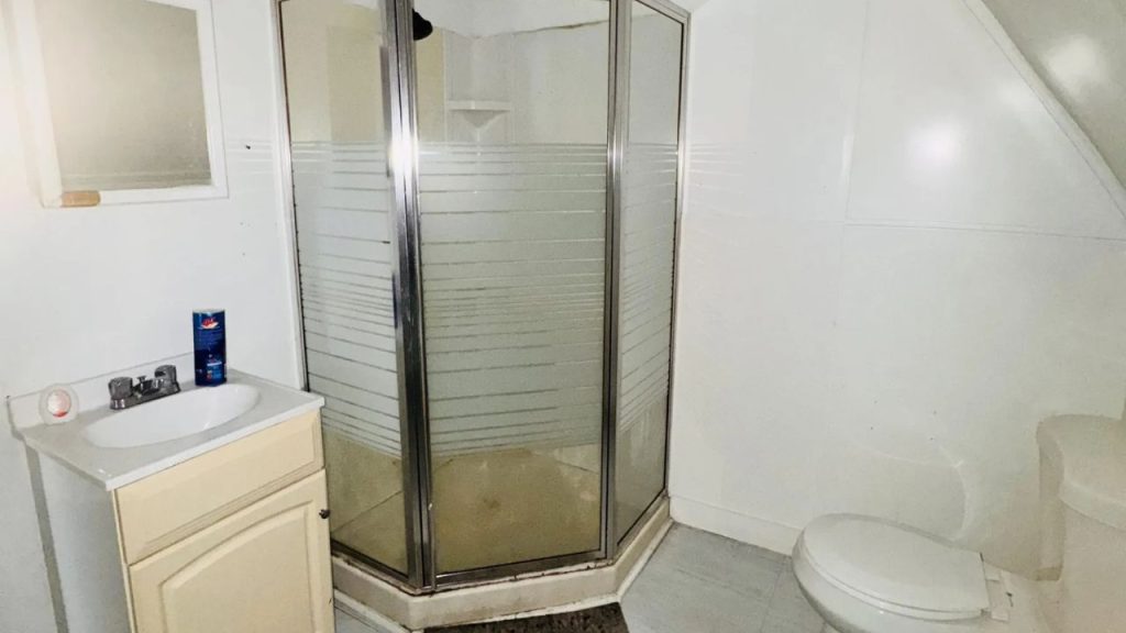 A cozy bathroom with a glass shower, small vanity, and slanted ceiling.
