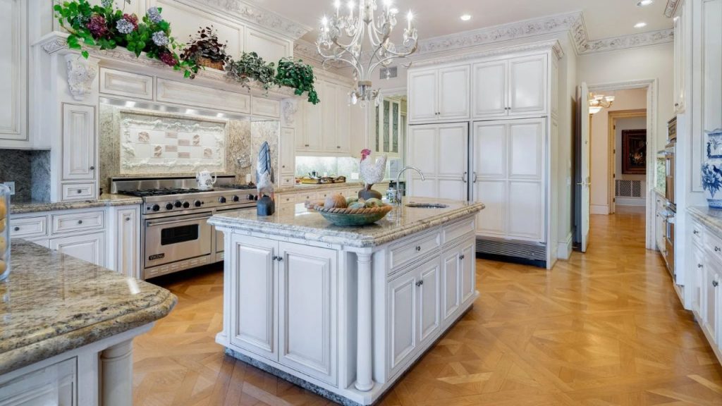 A stylish kitchen with a chandelier, granite island, and white cabinetry.