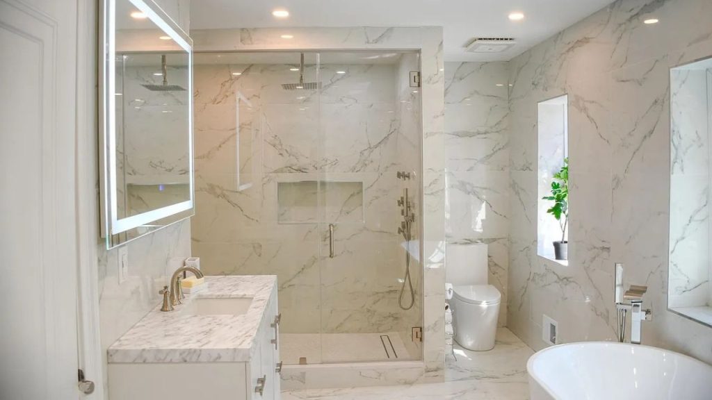 A luxurious bathroom with marble walls, a glass shower, soaking tub, and potted plants by the window.