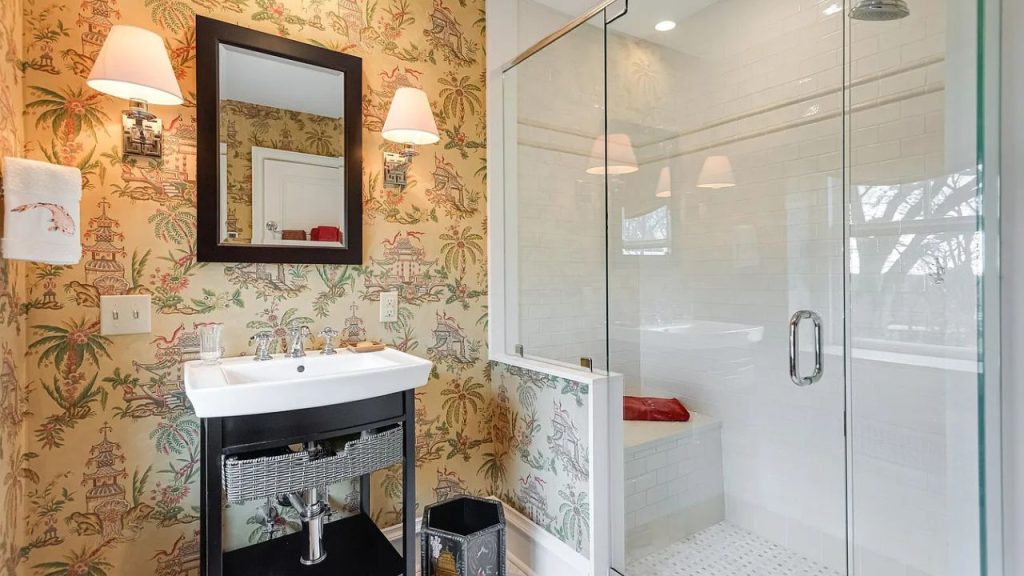 A stylish bathroom with tropical wallpaper, a glass shower, and elegant lighting.