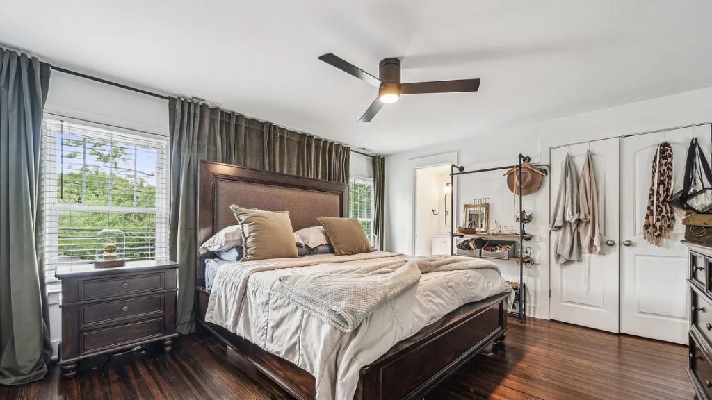 A serene bedroom with a wooden bed, green curtains, and a ceiling fan.