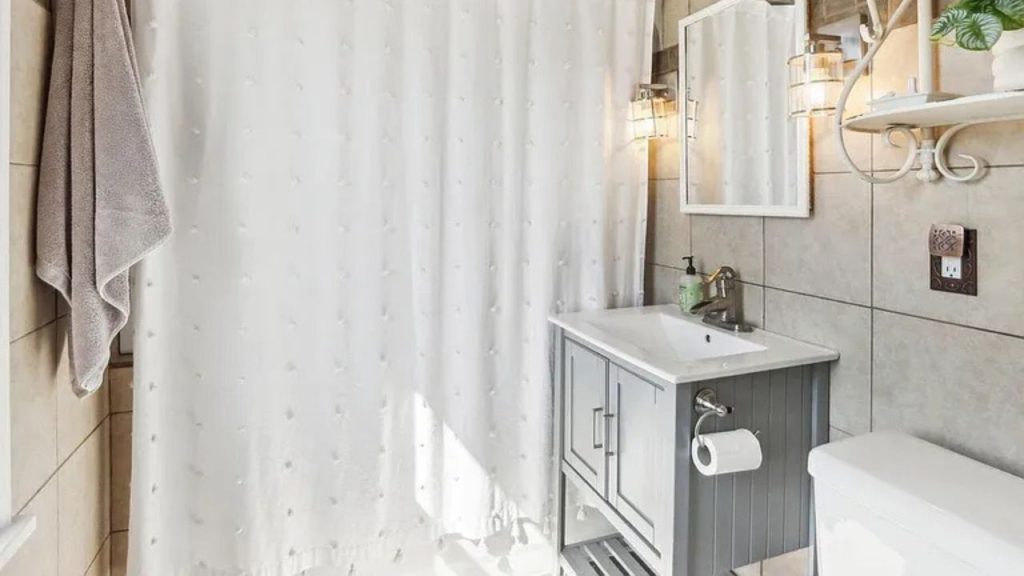 A serene bathroom with a white shower curtain, gray vanity, and elegant wall sconces.
