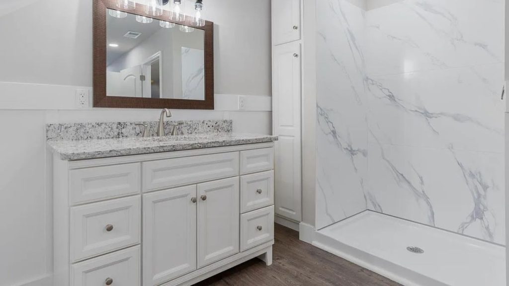 An elegant bathroom with a marble shower, double vanity, hardwood floors, and stylish lighting.