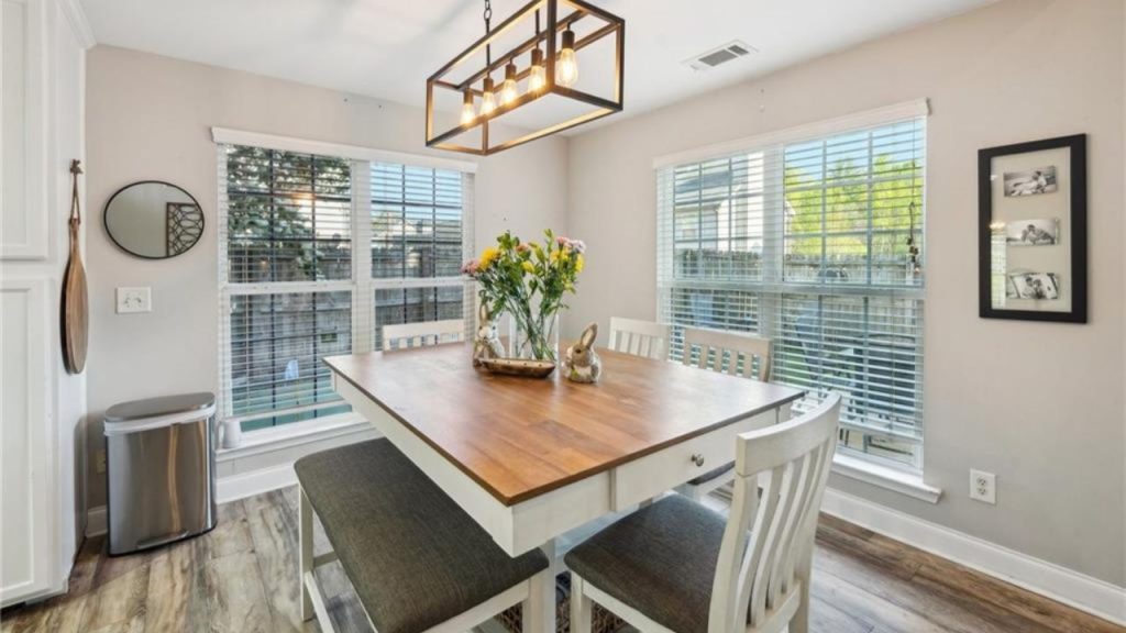 A cozy dining area with a wooden table, cushioned benches, pendant light, and large windows.