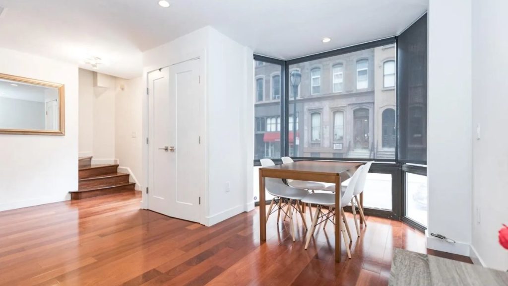 Dining area with wood table, white chairs, and large corner windows overlooking the street.