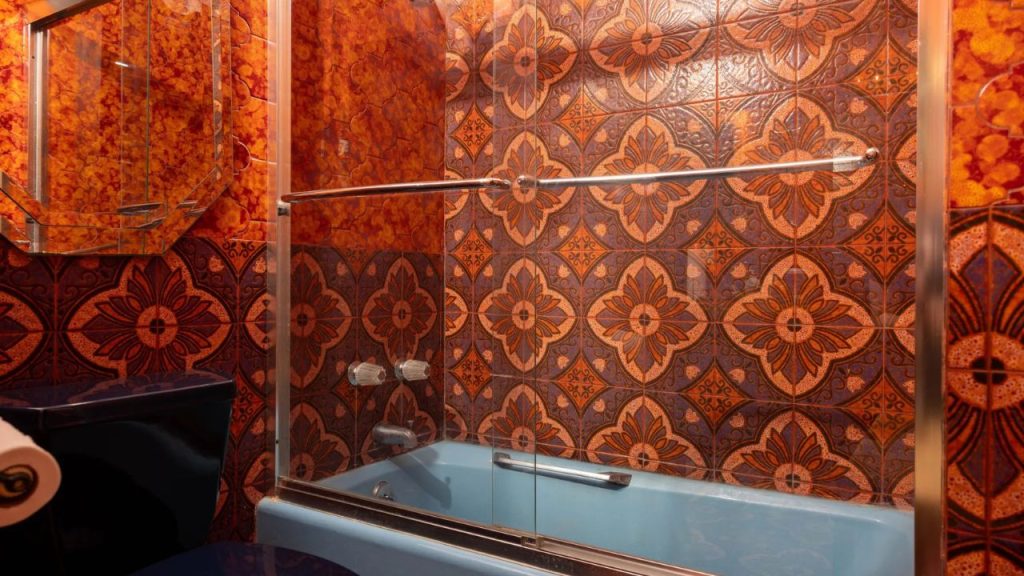 Retro bathroom with bold patterned tiles, a blue bathtub, and a glass shower door.