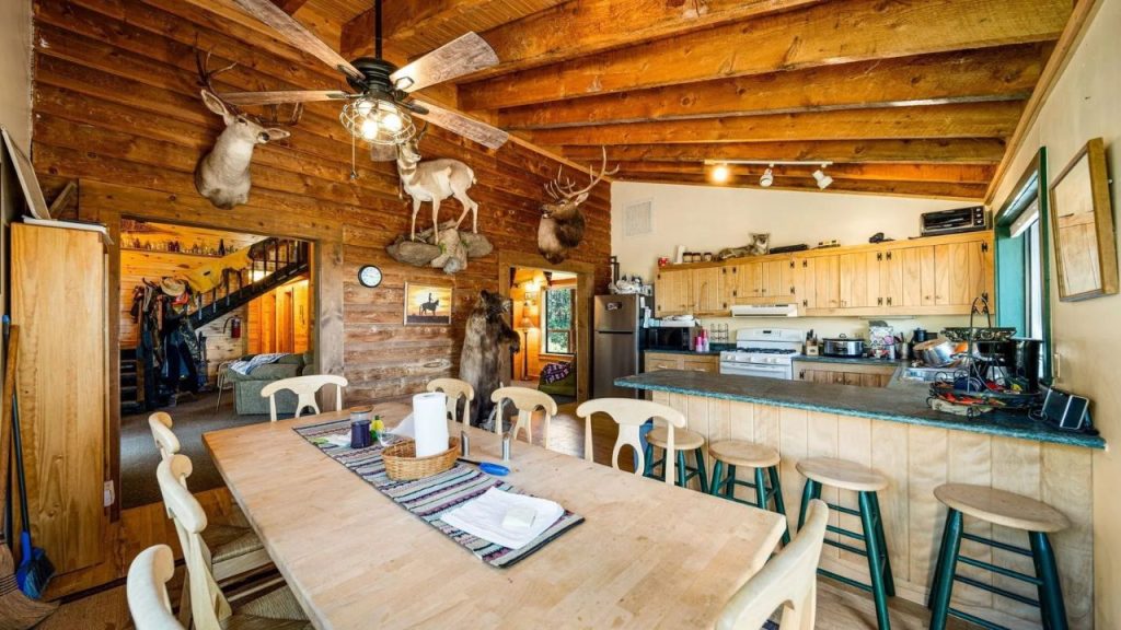 Rustic cabin kitchen and dining room with wood walls, taxidermy decor, and open beams.