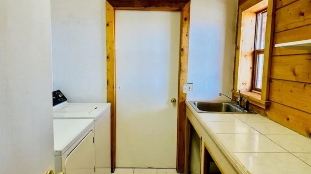 Laundry room with washer, tiled counter, and wood trim accents.