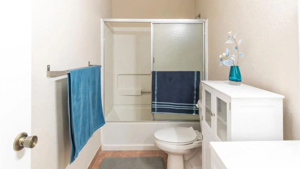 A serene bathroom with beige walls, white vanity, blue vase, glass shower, and terracotta tiles.