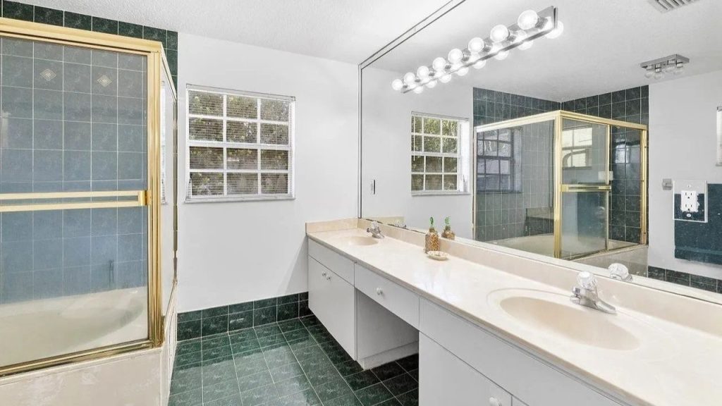 A bright bathroom with green tiles, dual sinks, and glass showers.