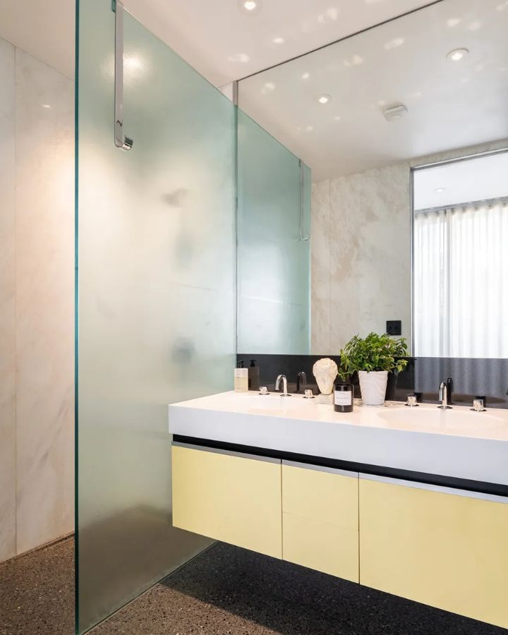 Bright bathroom with pastel yellow vanity and frosted glass divider.