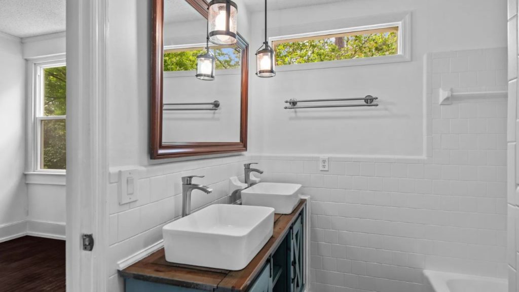 White bathroom with double sinks and wood accents.