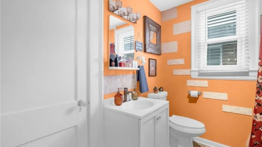 Cheerful orange bathroom with eclectic wall decor and white vanity.