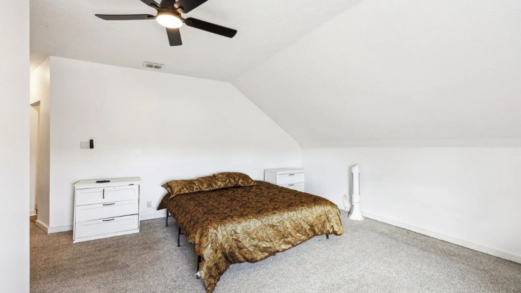 Minimalist attic bedroom with sloped ceiling, bronze bedding, and white nightstands.