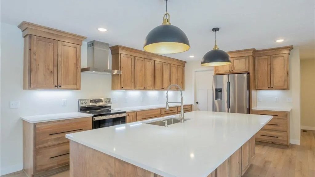 Kitchen with large white island, wood cabinets, and pendant lights.